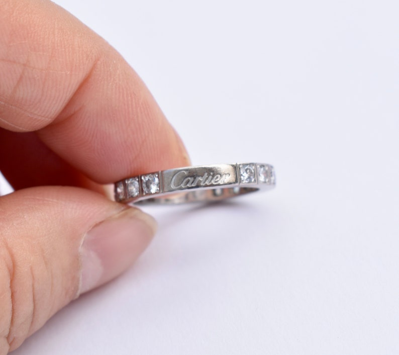 May include: A silver band ring with small diamonds set in the band and the word 'Cartier' engraved on the band.