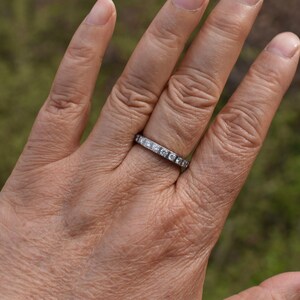 May include: A silver band with small, clear, square-shaped stones set in the band.
