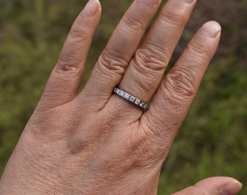 May include: A silver band with small, clear, square-shaped stones set in the band.