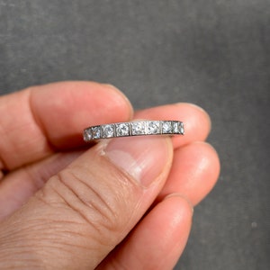 May include: A silver band with a row of small, square-shaped diamonds
