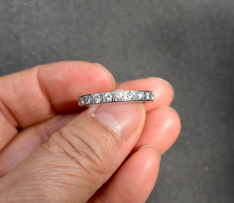May include: A silver band with a row of small, square-shaped diamonds