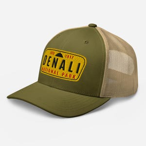 May include: A green and tan trucker hat with a yellow patch that says "ESTD 1917 DENALI NATIONAL PARK" in red and black lettering.
