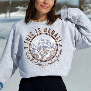 May include: A gray sweatshirt with a brown graphic print of a mountain range and the text "This is Denali Keep McKinley in history books".