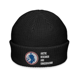 May include: Black knit beanie with a folded brim. The beanie features an embroidered patch with a globe design and the words "ARCTIC RESEARCH AND CONSERVATION" in white text. The hat is a winter accessory.