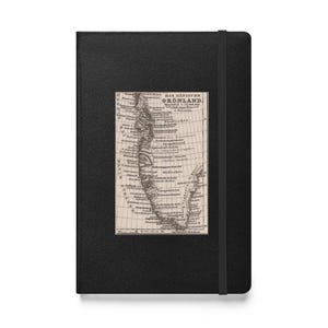 May include: A black journal with an elastic band closure. A rectangular map of Greenland, with text in German, is affixed to the front cover. The map is in shades of beige and brown.