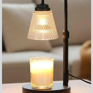 Peut inclure: Une lampe chauffe-bougie noire avec un abat-jour en verre transparent à motif de losanges et une bougie allumée dans un pot en verre. La lampe a un bras courbé et une base ronde.