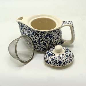 Può includere: Teiera in ceramica con motivo floreale blu e bianco. Include un coperchio e un infusore per tè in acciaio inossidabile. Il manico e il beccuccio sono biancastri. La teiera è progettata per preparare il tè.