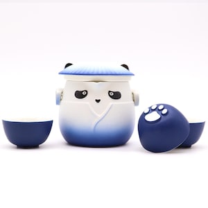 May include: A panda-themed tea set. The set includes a teapot with a lid, two small teacups, and a round container with a paw print. The teapot and cups are white and blue, with a gradient effect.