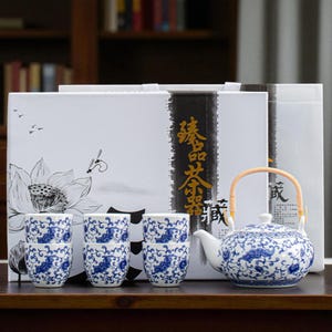 Peut inclure: Service à thé en céramique blanc et bleu, comprenant une théière et six tasses. La théière a une anse en bambou et un motif floral bleu. Les tasses présentent le même motif floral bleu. L'ensemble est présenté avec une boîte décorative.