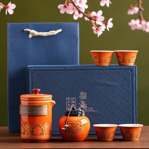 May include: An orange tea set with gold floral patterns, including a teapot, small jar, and teacups. The set is presented with a blue gift box and bag, and is decorated with cherry blossoms.