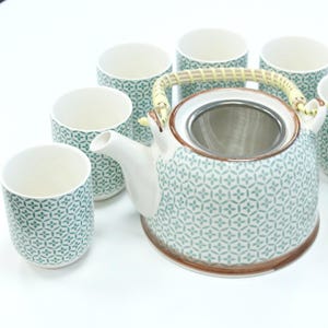 May include: A ceramic tea set featuring a teapot and matching cups. The teapot has a woven handle and a built-in strainer. The set is decorated with a teal and white geometric pattern. The cups are cylindrical and have the same pattern.