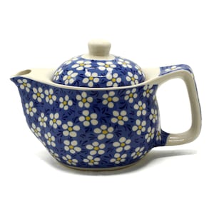 May include: A blue ceramic teapot with a white floral pattern and a matching lid. The teapot has a curved handle and spout, and the lid has a small knob. The teapot is designed for brewing tea.