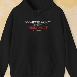 Peut inclure: Sweat-shirt à capuche noir avec le texte "WHITE HAT BY DAY RED HAT BY NIGHT" imprimé sur le devant.