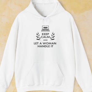 May include: White hoodie with a black graphic print that says "Keep Calm and Let a Woman Handle It". The graphic also includes a laptop with a crown on top and two branches of leaves.