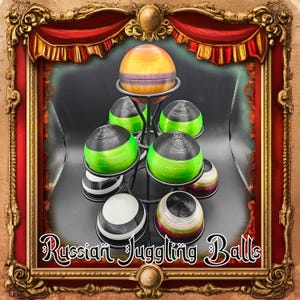 May include: A display of Russian juggling balls in various colors, including green, black, white, and striped patterns. The balls are arranged on a black metal stand. The text "Russian Juggling Balls" is displayed at the bottom.