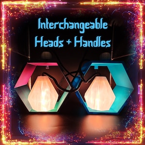 Op de afbeelding: Twee moderne lampen met verwisselbare koppen en handvatten. Elke lamp heeft een geometrisch, zeshoekig frame in roze en teal, met een witte, facetgeslepen kap. De tekst "Interchangeable Heads + Handles" wordt boven de lampen weergegeven.