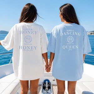 May include: Two oversized t-shirts, one white and one light blue, with text and a globe graphic on the back. The white shirt says "I FOUND MY HONEY" and the blue shirt says "BIANCA'S DANCING QUEEN".