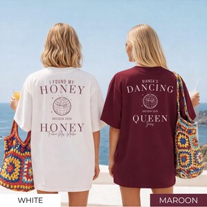 May include: Two oversized t-shirts, one white and one maroon, with text and graphic designs on the back. The white shirt says "I FOUND MY HONEY" and "HONEY" with a globe graphic. The maroon shirt says "BIANCA'S DANCING QUEEN".