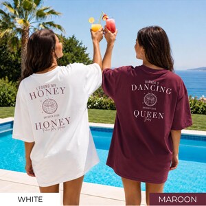 May include: Two oversized t-shirts, one white and one maroon, with text on the back. The white shirt says "I FOUND MY HONEY" with "DRESDEN 2026" and "HONEY" below. The maroon shirt says "BIANCA'S DANCING QUEEN" with "DRESDEN 2026" and "Joly" below.