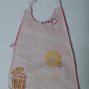 May include: A baby bib with a pink and white striped design, featuring a red fishbone, a yellow circle, a star, and a trash can illustration. The bib has a red trim and a white neckband.