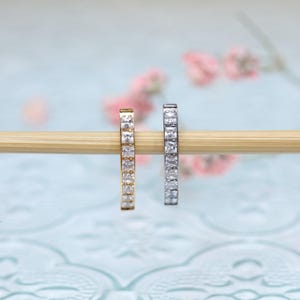 May include: Two hoop earrings with a row of clear cubic zirconia stones. The hoop on the left is gold and the hoop on the right is silver.