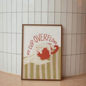 May include: A framed print with a red cup overflowing with white foam. The text "My Cup Overflows" is written in a pink cursive font around the cup.