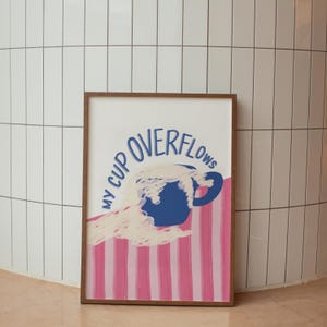 May include: A framed print with a blue cup overflowing with white liquid. The text "My Cup Overflows" is written in a blue cursive font around the cup. The background is a pink and white striped pattern.