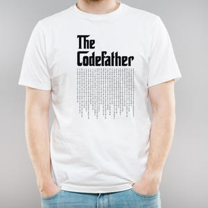 Op de afbeelding: Wit T-shirt met zwarte tekst die "The CodeFather" zegt en een patroon van binaire code eronder.