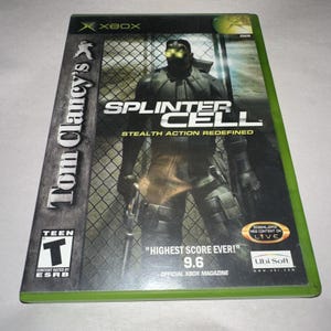 May include: A Tom Clancy's Splinter Cell video game case for the original Xbox console. The cover features a character in black tactical gear with glowing green goggles, standing before a chain-link fence. Text includes Stealth Action Redefined.