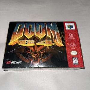 May include: A sealed Doom 64 video game box for the Nintendo 64 console. The black box features the gold Doom 64 logo, a demonic creature illustration, and the Midway logo. The right side has a red vertical strip with the Nintendo 64 logo and ESRB M rating.