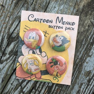 May include: A set of four cartoon character button pins. The pins are on a card that says "Cartoon Menko Button Pack". The characters are a duck, a dog, a cat, and a pig. The buttons are colorful and have a vintage look.