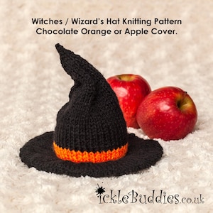 May include: A black knitted witch's hat with an orange band, beside two red apples. The hat is the main subject, with the text "Witches / Wizard's Hat Knitting Pattern Chocolate Orange or Apple Cover."