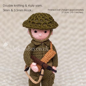 May include: A crocheted doll soldier wearing a green uniform, a brown belt, and a green helmet. The doll is holding a brown rifle and is approximately 10-11 inches tall.