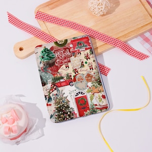 Può includere: Una custodia per tablet con un design natalizio festivo. La custodia presenta un collage di immagini natalizie, tra cui Babbo Natale, alberi di Natale e le parole "Hot Cocoa". Gli accenti rossi e verdi sono prominenti.