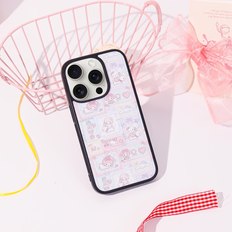 Op de afbeelding: Een zwart-witte telefoonhoes met een kleurrijk patroon van cartoonfiguren, harten en andere schattige ontwerpen. De hoes heeft een zwarte rand en bedekt de achterkant en zijkanten van de telefoon. De telefoonhoes ligt op een wit oppervlak.