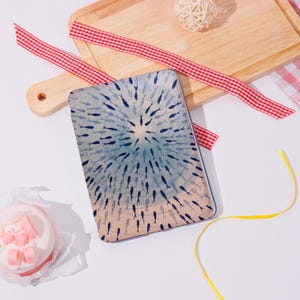 Könnte beinhalten: Rechteckige dekorative Platte mit einem Fischmuster in Blau- und Beigetönen, angeordnet in einem kreisförmigen Muster. Die Platte liegt auf einer weißen Oberfläche mit einem Holzschneidebrett, rot-weißem Band und einem kleinen Kuchen.