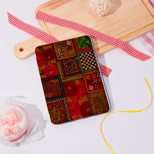 May include: A patterned tablet case with a patchwork design in red, green, and brown. The case features floral, paisley, and checkered squares. A red and white gingham ribbon and a yellow ribbon are also in the image. The case is rectangular.