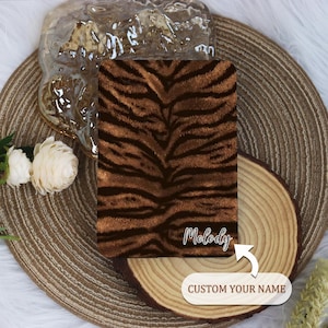 Peut inclure: Un tissu à imprimé zèbre brun et noir avec le nom "Melody" écrit en blanc. Le texte "CUSTOM YOUR NAME" est écrit sous le nom.