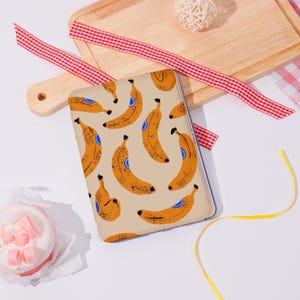 Peut inclure: Une coque de téléphone beige avec un motif répété de bananes oranges avec des détails bleus. L'étui rectangulaire a une bordure transparente. Le design est une interprétation ludique et moderne d'un thème tropical.