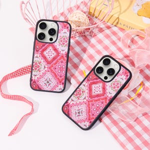 May include: Two phone cases with a pink and red floral pattern. The cases have a black border and a design featuring squares, hearts, and flowers. The cases are on a pink and white checkered surface.