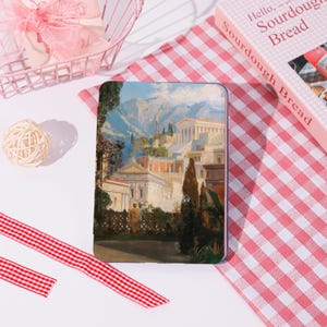 May include: A tablet case featuring a classical landscape painting with buildings, trees, and mountains. The case is rectangular and has a colorful image. The case is on a red and white checkered surface.
