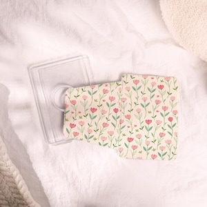 Könnte beinhalten: Eine transparente Handyhülle mit einem floralen Einsatz. Der Einsatz zeigt ein Muster aus rosa Tulpen mit grünen Stielen und Blättern auf cremefarbenem Hintergrund. Die Hülle ist offen und zeigt den Einsatz.