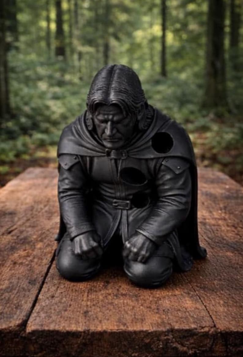 May include: A matte black sculpture of a kneeling figure with long hair, wearing a cloak and tunic. The figure has a somber expression with hands clenched in front of the knees. Several circular voids are visible on the chest and shoulder area.