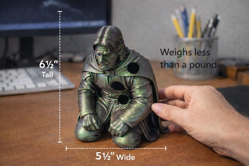 Op de afbeelding: Een knielend beeldje van een man in een mantel, ongeveer 16,5 cm hoog en 14 cm breed. De figuur heeft een metallic groene en zilveren afwerking. De tekst in de afbeelding luidt: "Weegt minder dan een pond."