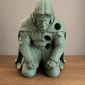May include: A monochromatic light green figurine of a kneeling person with long hair, wearing a collared tunic and a cape. The figure features three circular holes positioned on the left shoulder, the chest, and the waist area of the garment.