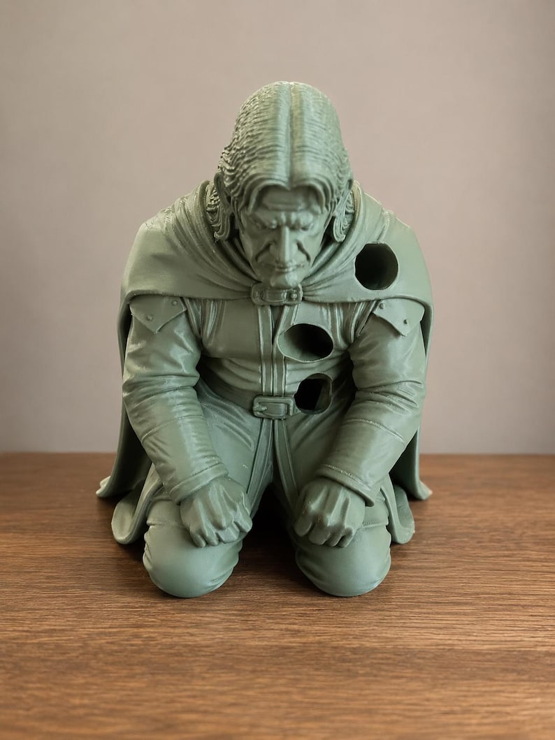 May include: A monochromatic light green figurine of a kneeling person with long hair, wearing a collared tunic and a cape. The figure features three circular holes positioned on the left shoulder, the chest, and the waist area of the garment.