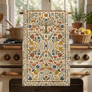 Puede incluir: Un pa&ntilde;o de cocina decorativo con un dise&ntilde;o caprichoso. El pa&ntilde;o presenta un motivo central de &aacute;rbol rodeado de setas, ciervos, zorros, limones y flores en tonos naranja, azul y amarillo sobre un fondo crema. El pa&ntilde;o est&aacute; colgado de una barra de madera.