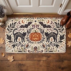 以下が含まれることがあります： クリーム色の背景にハロウィーンをテーマにした左右対称のイラストが描かれた長方形のドアマット。中央のオレンジ色のジャック・オー・ランタン、2匹の黒猫、2匹のコウモリ、2羽のフクロウ、小さな家、クモの巣、植物の模様がデザインされています。