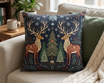 May include: A square throw pillow featuring a dark blue background with two symmetrical brown deer facing each other. The design includes green pine trees, white snowflakes, and floral patterns. The pillow is placed on a light-colored sofa.