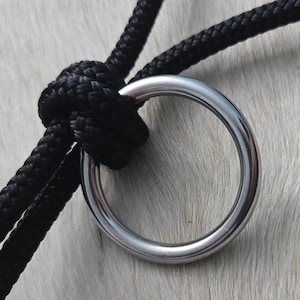 May include: A black rope with a silver metal ring. The rope is tied in a knot around the ring.